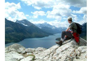 man sitting on mountain top looking over lakeview